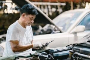 Garage Asian professional working auto service checking engine. Mechanic man using tablet computer t