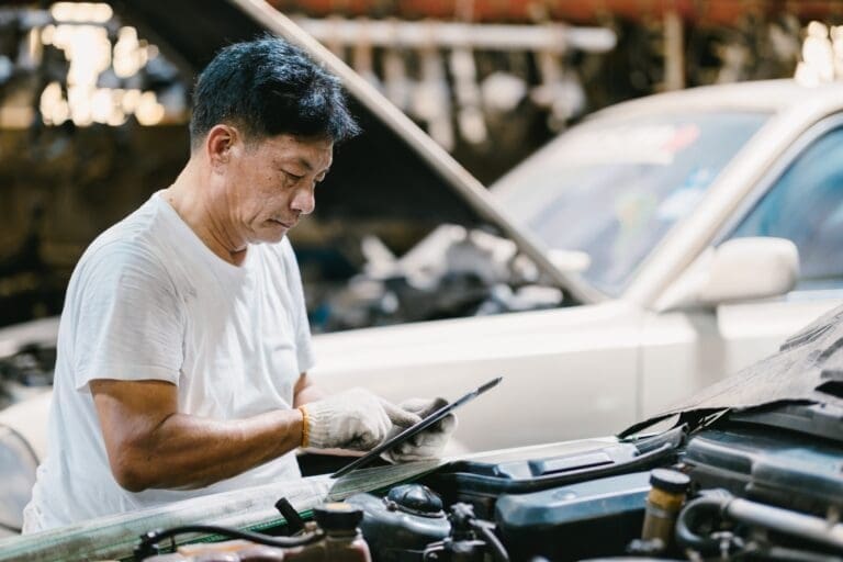Garage Asian professional working auto service checking engine. Mechanic man using tablet computer t