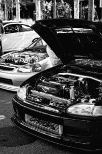 Two cars with hoods open showing engines